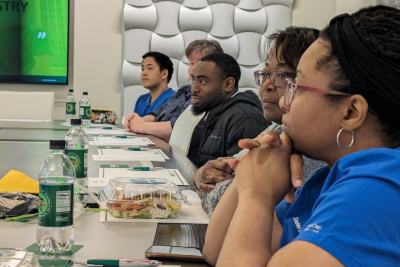 a Group of people sitting at conference table in a conference setting listening to an offscreen speaker with UAB water bottles and lunch in front of them